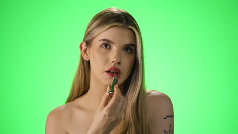 disparo medio de los labios de la mujer mientras se tocan con un lápiz labial rojo para aplicarlo con luz verde púrpura en su rostro de la joven mientras se está preparando en cámara lenta