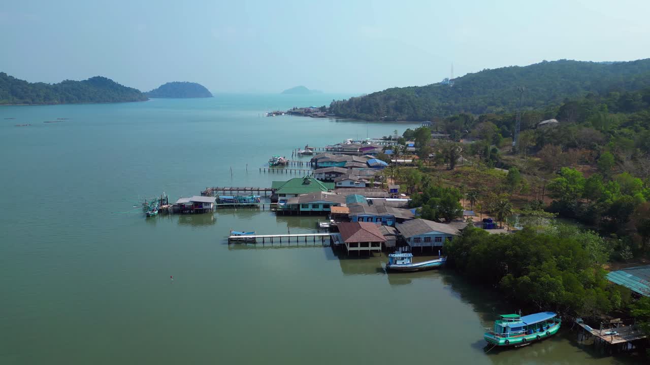 Coastal village with houses on stilts, boats and a long pier in a tropical bay. Majestic aerial view fly push forward overflight flyover drone