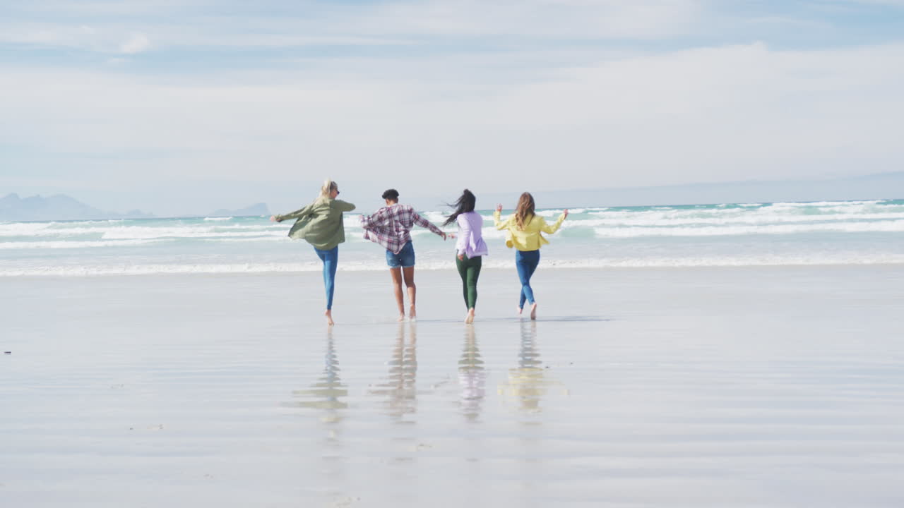 다양한 여성 친구들의 행복한 그룹이 해변에서 놀고 달리고 있습니다.
