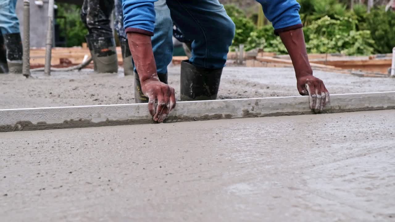 Laborer uses a large trowel to level the surface of freshly cast concrete