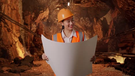 asian female engineer with safety helmet looking at blueprint in her hands and looking around in underground mine tunnel
