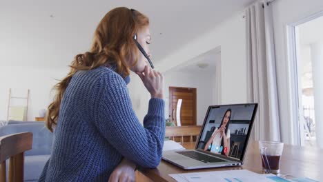 Caucasian-woman-using-laptop-and-phone-headset-on-video-call-with-female-colleague