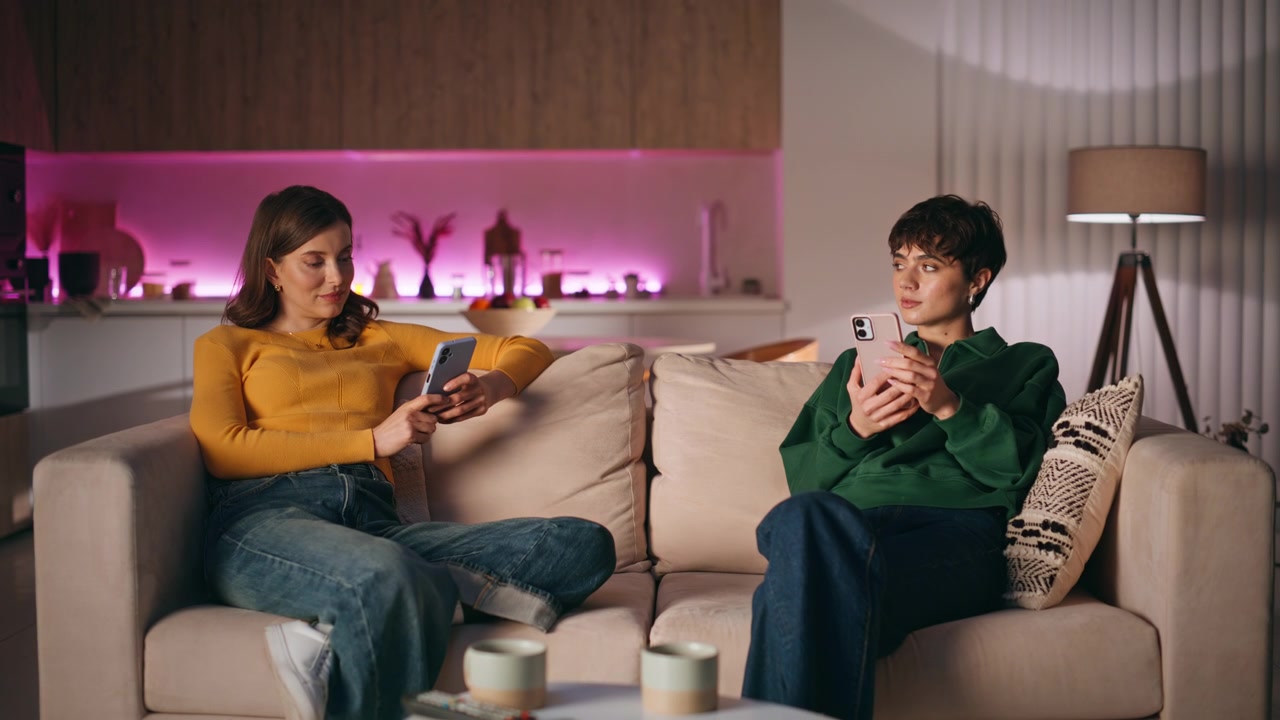 Separate couple browsing mobile phones sitting comfortable apartment couch.