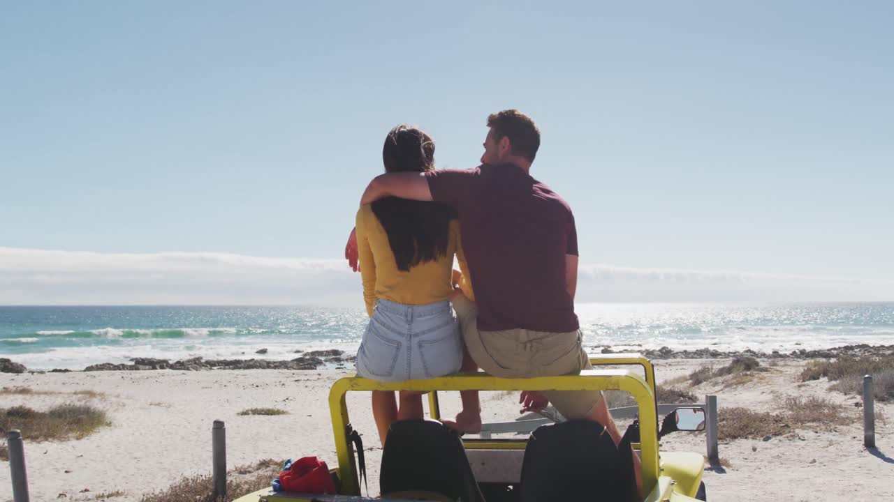 feliz pareja caucásica sentada en un buggy de playa junto al mar hablando