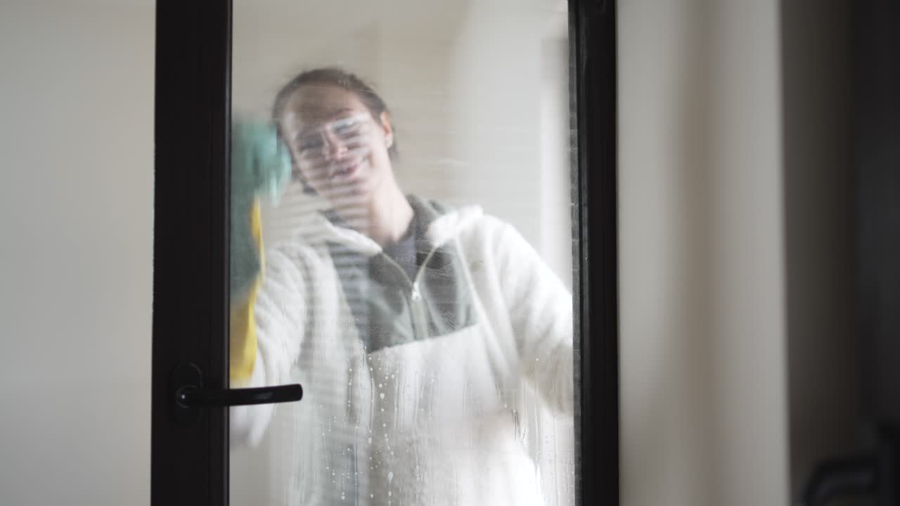 Scena di pulizia domestica che mostra una donna che pulisce finestre di vetro con spray e guanti, a simboleggiare rinnovamento, freschezza e igiene domestica