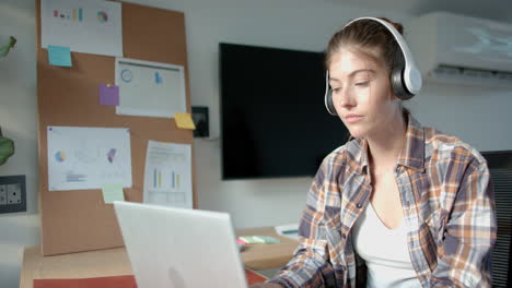 Wearing headphones, woman working on laptop at home office desk