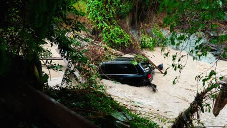 a car caught in a creek with muddy water rushing around it