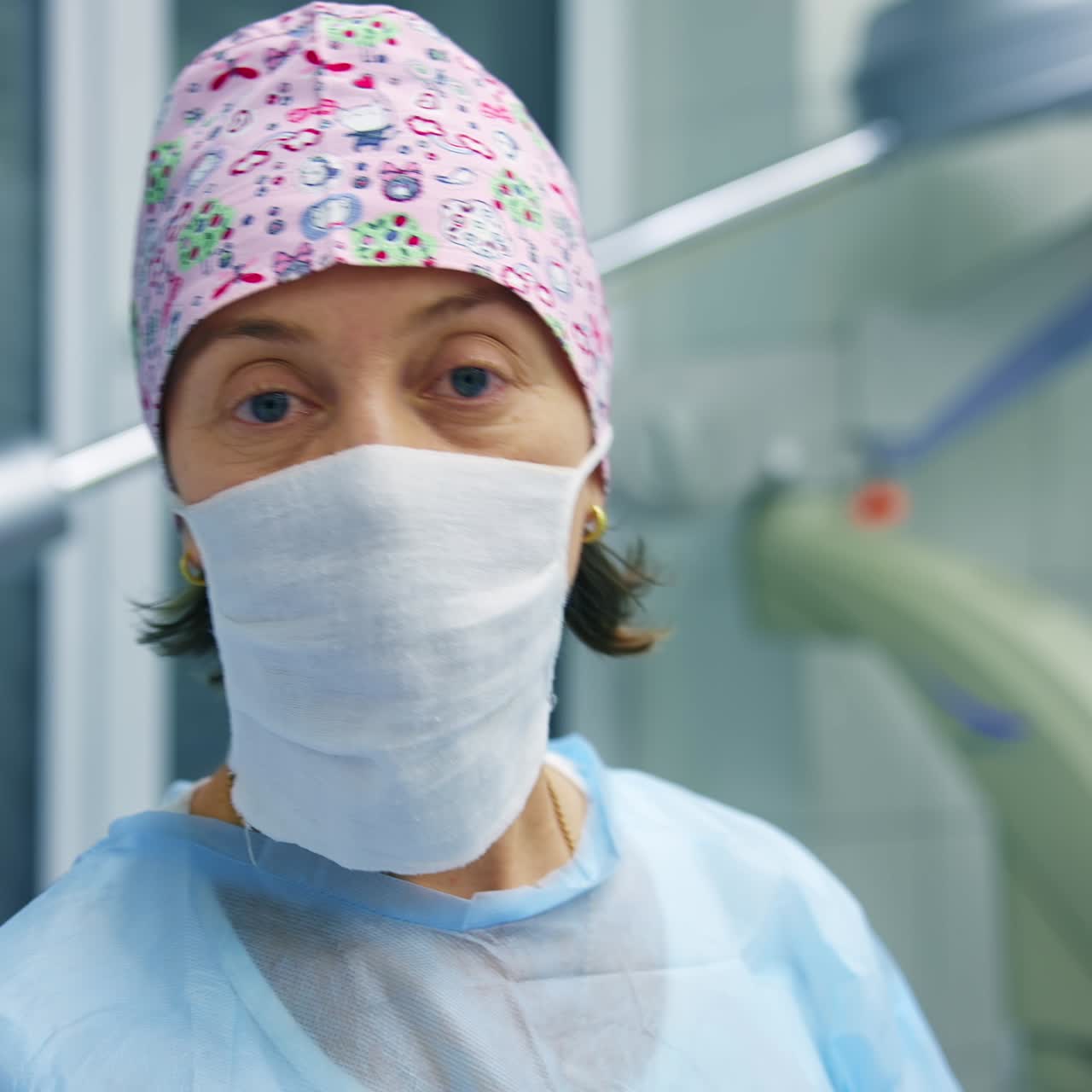 Professional ophthalmologist discusses surgery operation to the camera. Woman medic in scrubs and mask stands on modern equipment background