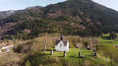 toma de drones de una capilla en la cima de una colina frente a las montañas alpinas