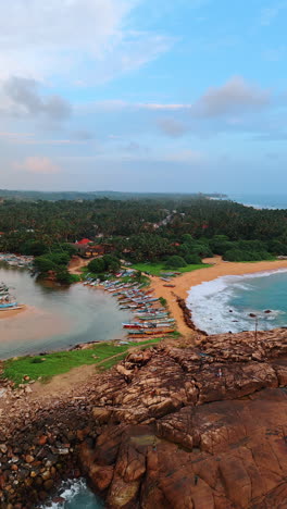 the indian ocean shore at the coast of sri lanka. multiple traditional asian boats stand on the sandy beach. aerial perspective on the village hiding in the tropical forests. vertical video.