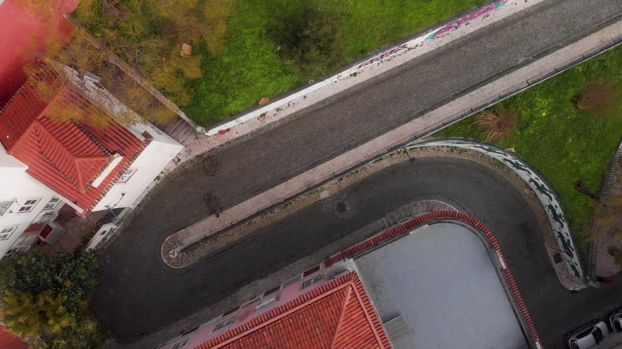 Panoramica dall'alto con drone sopra i tetti che segue un'auto che guida su una strada stretta a Lisbona.