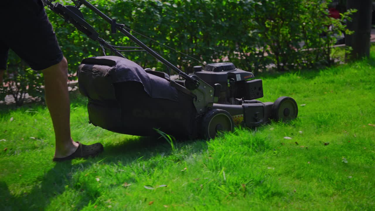 Person Mowing Green Grass with a Lawnmower in a Garden