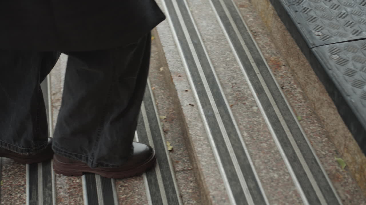 Closeup determined stride on steps, creator crossing threshold into foyer, wet grooves and metal nosing under leather boots, jeans sweeping, brisk purposeful movement, street to interior transition