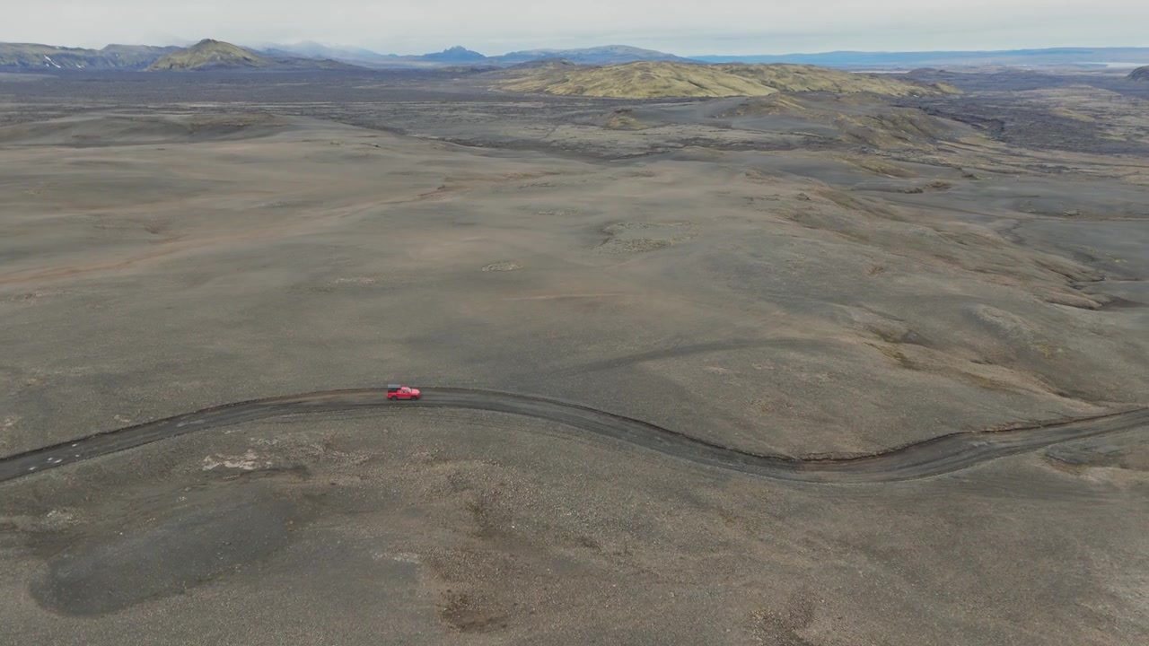 Veículo vermelho contornando uma trilha remota através de um vasto terreno vulcânico na Islândia, vista aérea da estrada F208