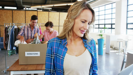 Mujer-Trabajando-En-Una-Computadora-Portátil-Mientras-Los-Voluntarios-Clasifican-La-Ropa-En-El-Fondo