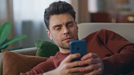 resting man surfing cellphone internet lying at home couch closeup. guy browsing