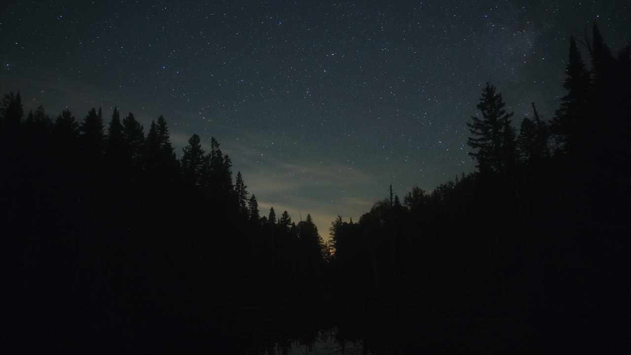 Timelapse from day to night over an autumn lake with Milky Way and cloudy sky in Mauricie, Quebec, Canada. Vibrant foliage and calm water create a peaceful, cinematic scene