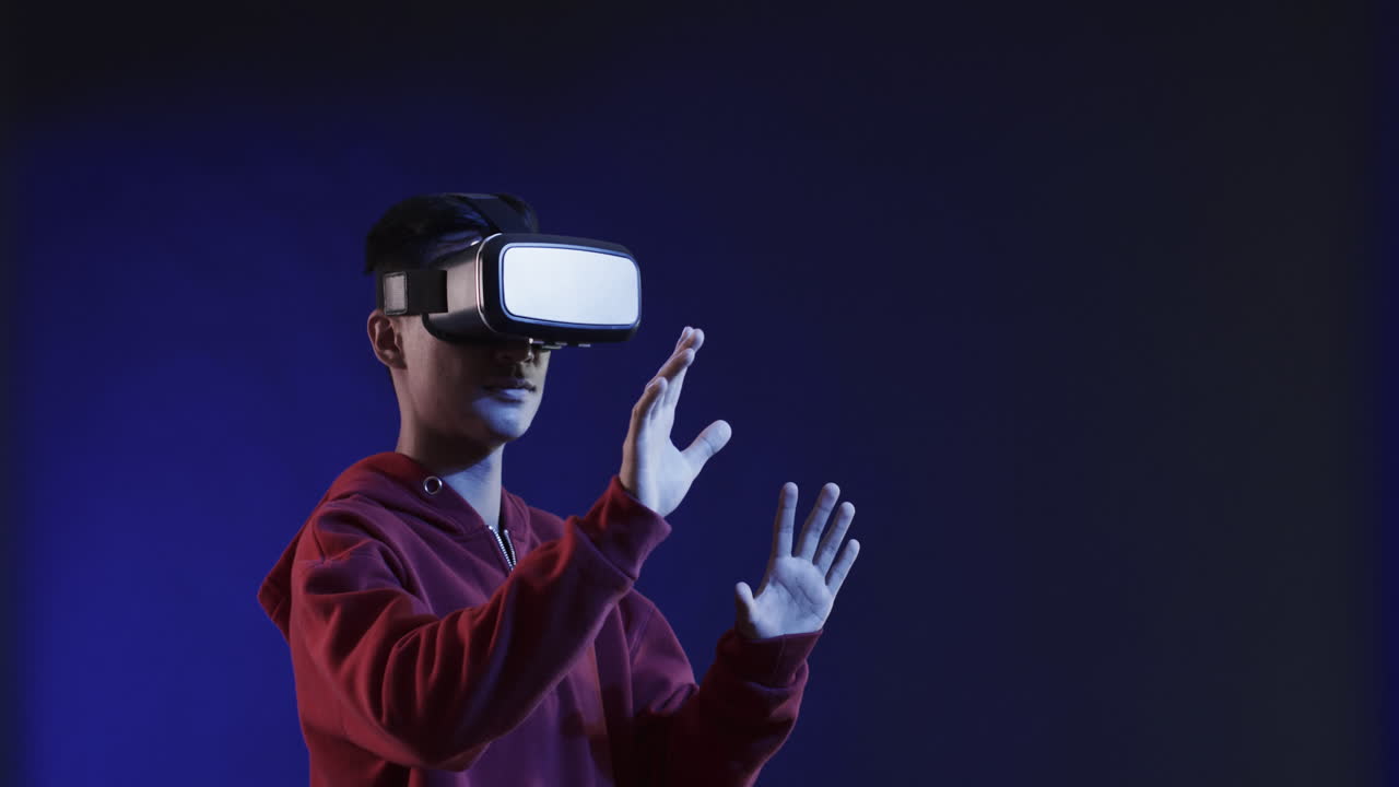 Asian man using vr headset, touching virtual screen on blue background, copy space, slow motion