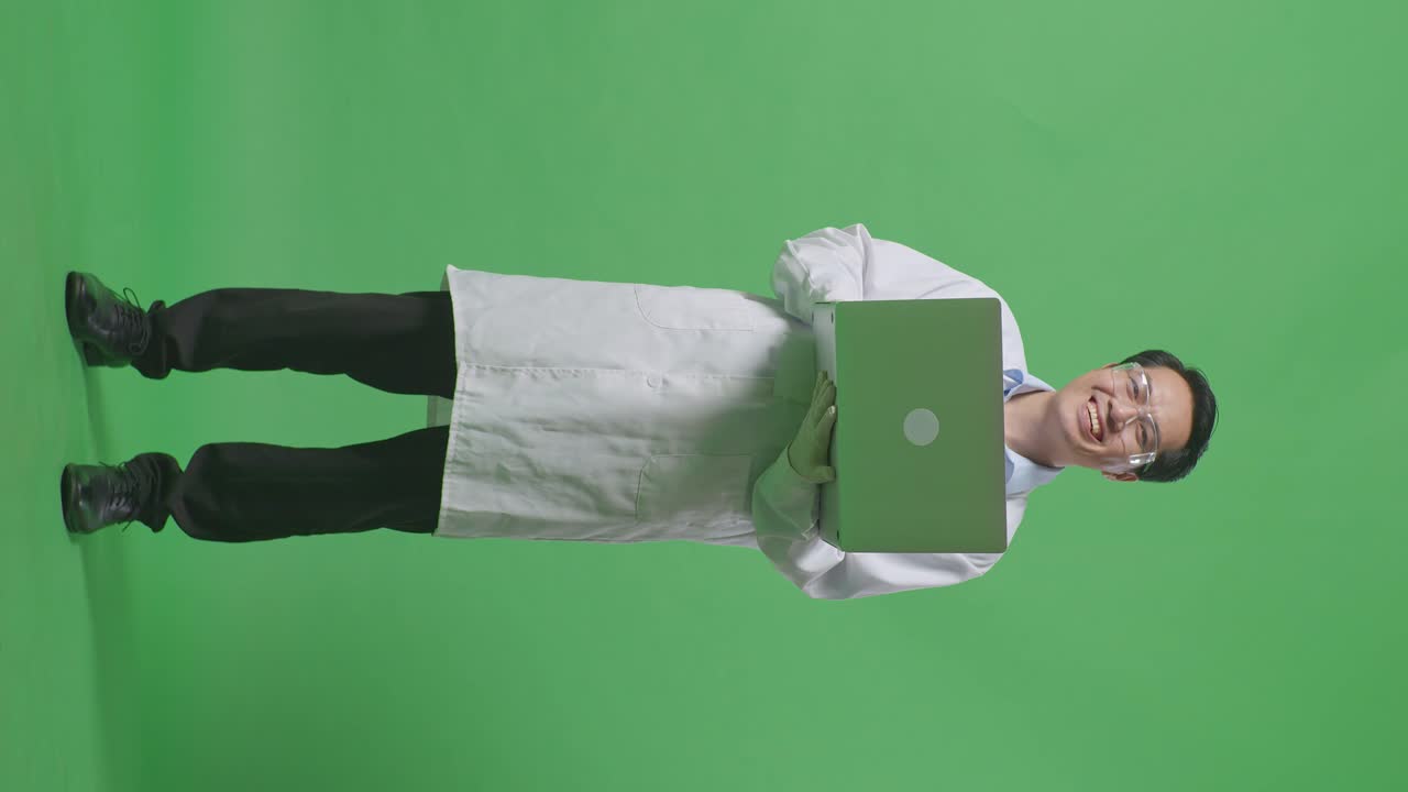 Full Body Of Asian Man Scientist Smiling To Camera While Standing And Working On A Laptop In The Green Screen Background Laboratory