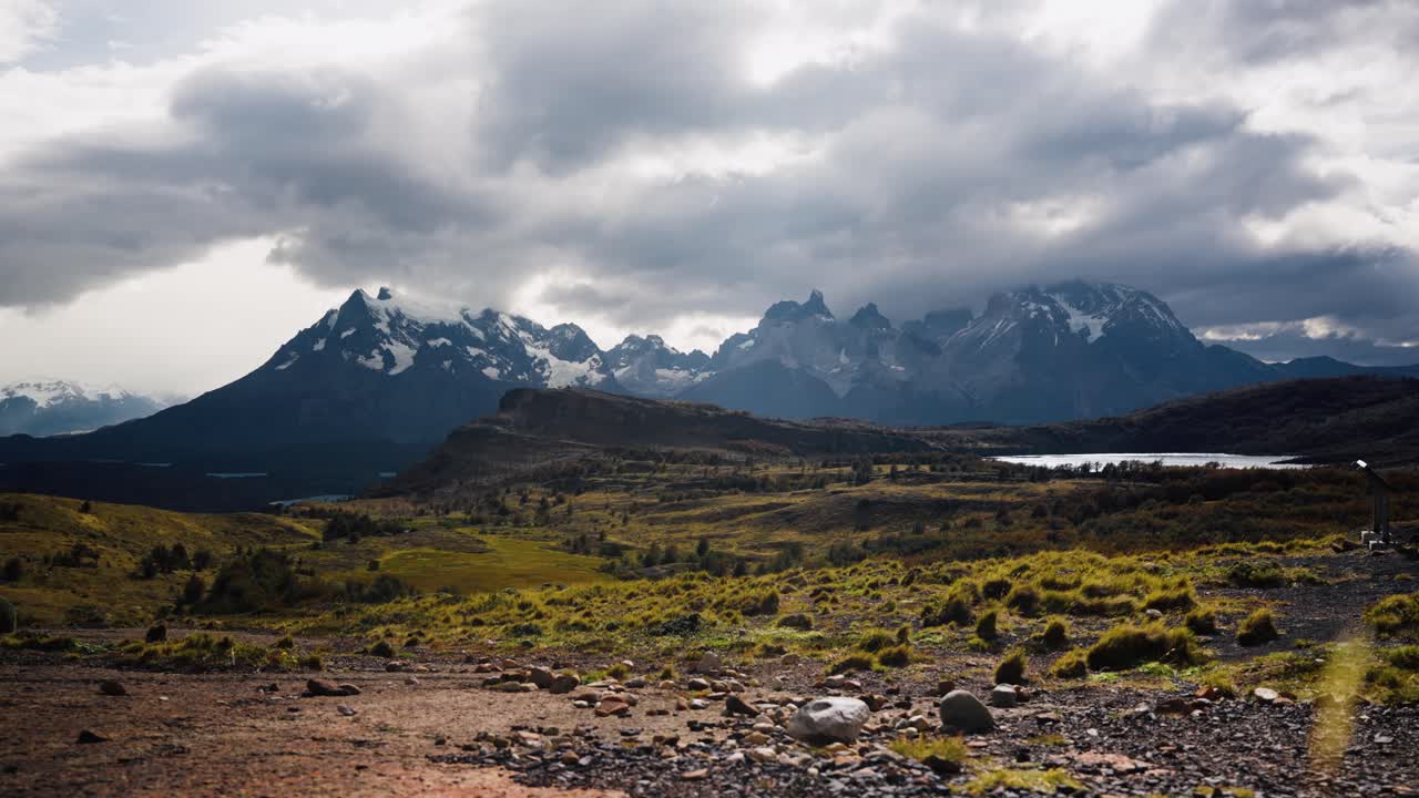 A lone trekker walks toward the Cuernos del Paine mountains in Patagonia under an overcast sky. Surrounded by vast wilderness, evoking solitude, adventure, and peaceful exploration.