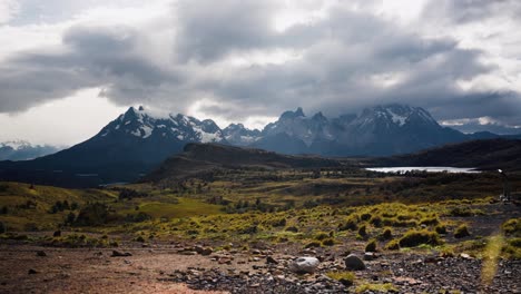 a lone trekker walks toward the cuernos del paine mountains in patagonia under an overcast sky. surrounded by vast wilderness, evoking solitude, adventure, and peaceful exploration.