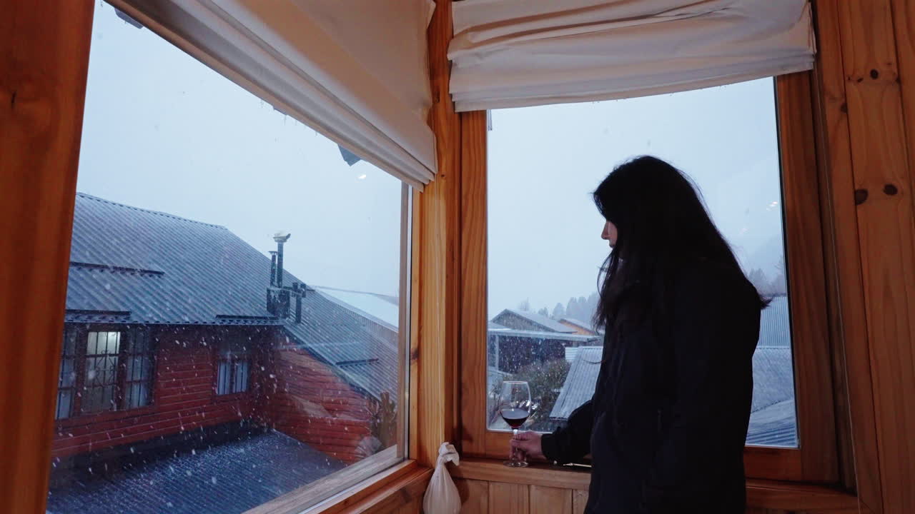 Relaxed woman enjoying wine while watching snowy winter view from hotel window, travel luxury