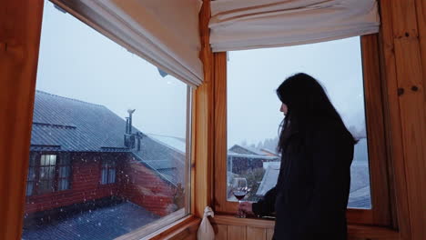 relaxed woman enjoying wine while watching snowy winter view from hotel window, travel luxury