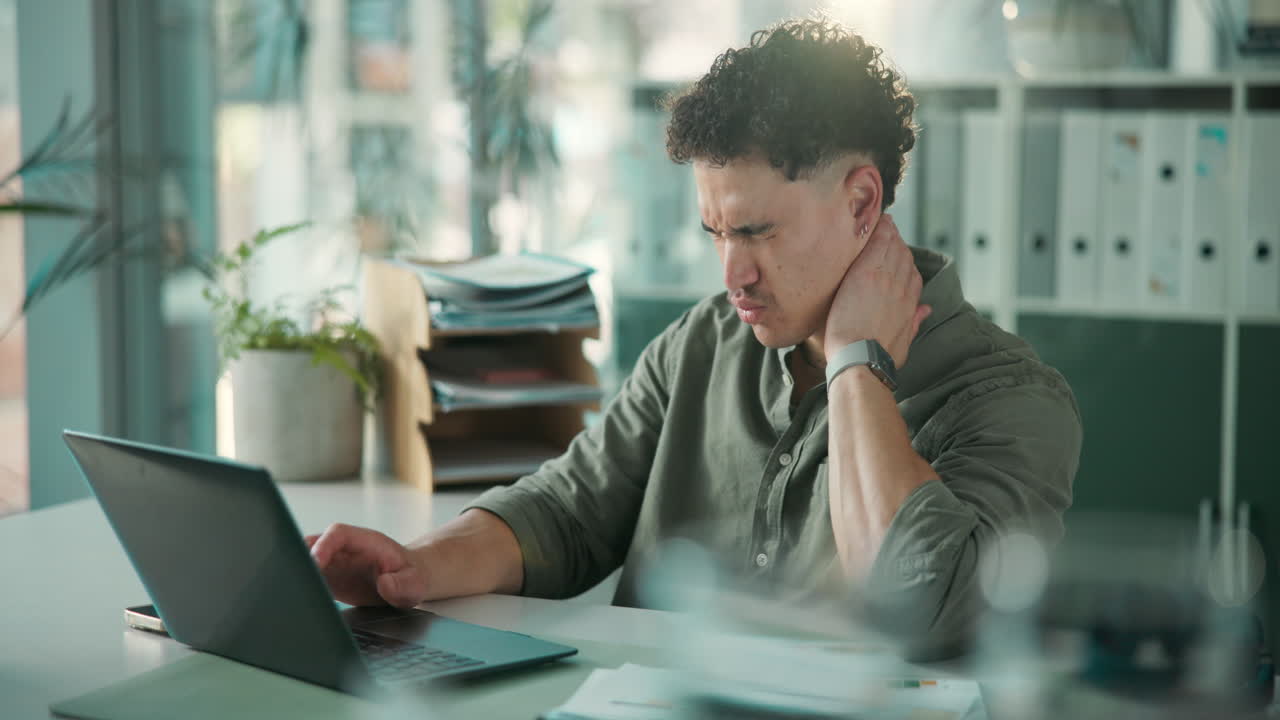 Young Man Experiences Neck Pain While Working on Laptop in Office