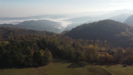 Top-of-the-mountain,-over-green-forest-to-the-fogy-valley---aerial