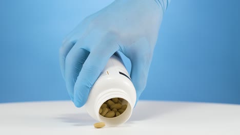 Studio-shot-hand-with-blue-gloves-pouring-vitamin-B12-pills-out-on-white-table