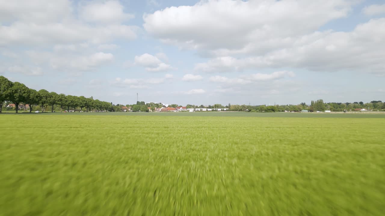 Aerial drone forward moving shot over green farmlands alongside a road in Brunswick, Germany on a sunny day