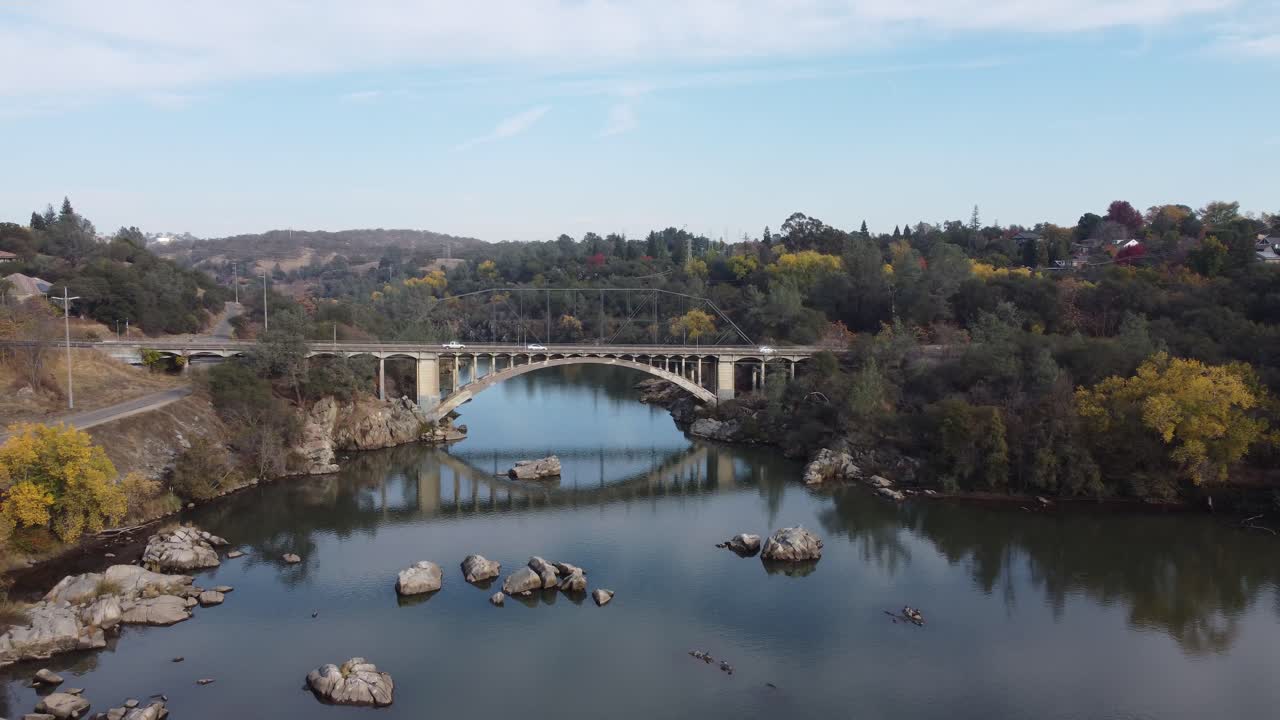 Beautiful traveling drone footage of arching bridge over still, reflective water revealing more and more of the surrounding environment