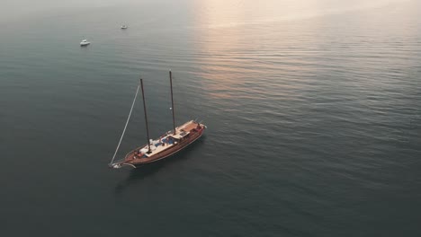 Aerial-of-two-friends-jumping-from-a-wooden-luxury-sailboat-during-sunset