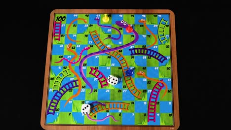 hands moving pieces on snakes and ladders board