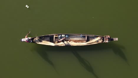 fishermen in small wooden boat row on dirty river in bangladesh