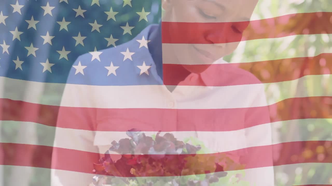 animación de la bandera de los estados unidos ondeando sobre una mujer afroamericana sonriente sosteniendo flores