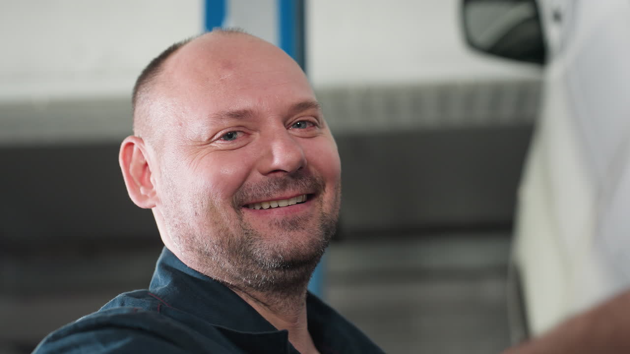 Close-up of engineer with a beaming smile in blue uniform and white gloves, adjusting car tires for alignment in an automotive workshop