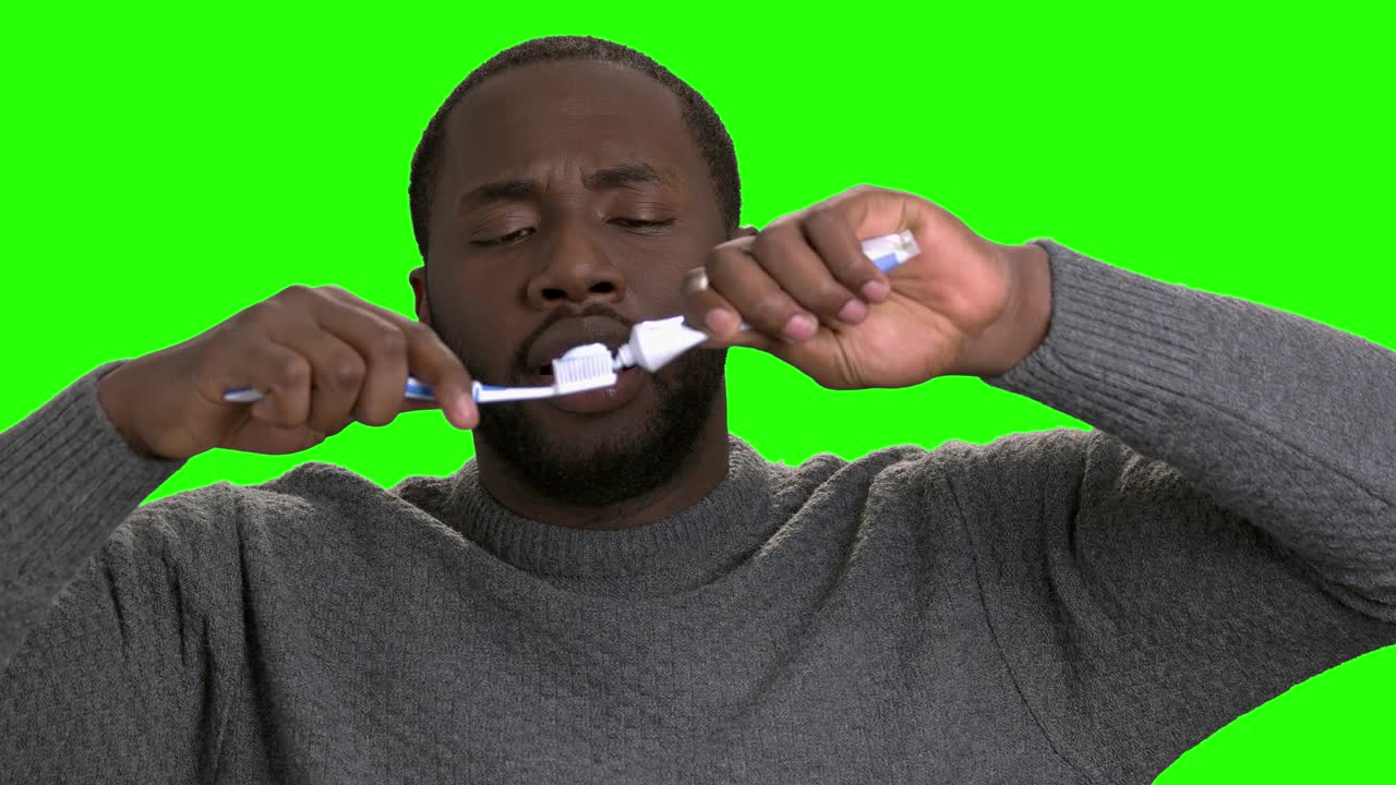 Dark-skinned man applying toothpaste on a toothbrush.