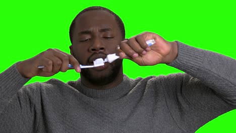 dark-skinned man applying toothpaste on a toothbrush.