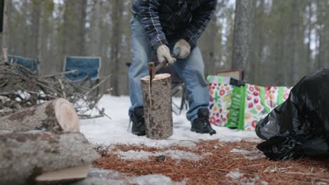 man slamming a log with an axe stuck in it into the snowy ground