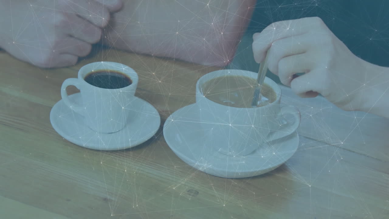 Two friends resting hand and stirring coffee on wooden table, displaying technology network overlay