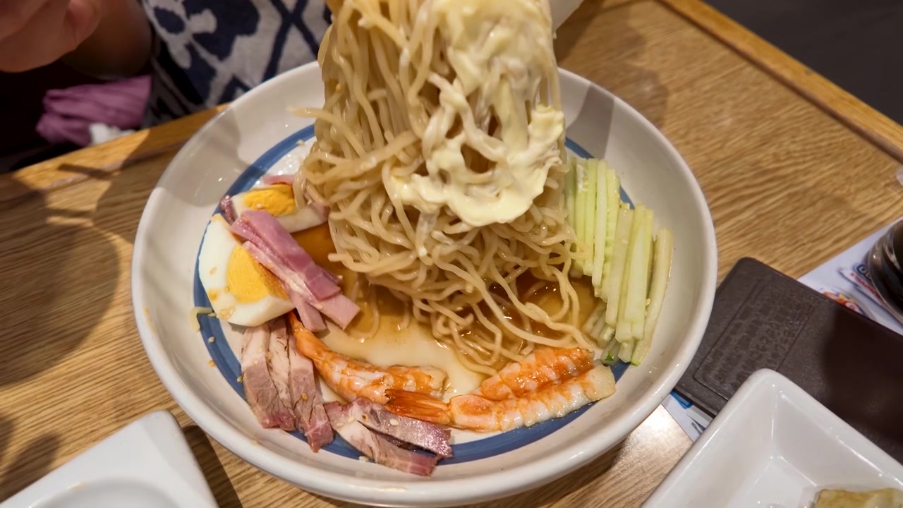 Primo piano di mani che usano le bacchette per sollevare spaghetti ramen da una ciotola con gamberetti