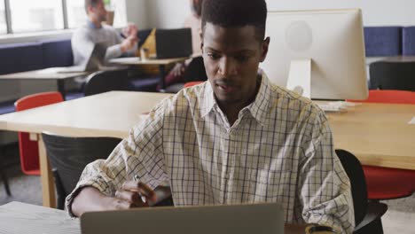 African-american-businessman-sitting-at-table-and-using-laptop-at-office