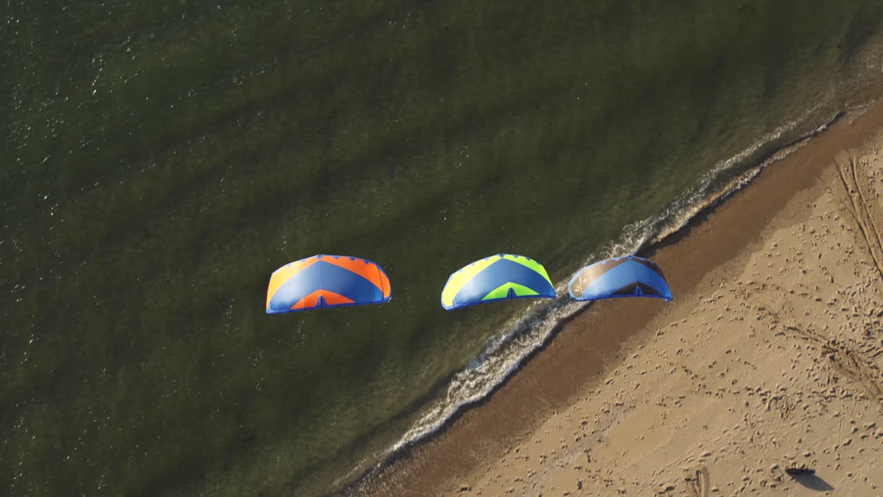kitesurfistas tumbados en la arena con cometas levantadas en el viento, en la costa de tweede maasvlakte, países bajos