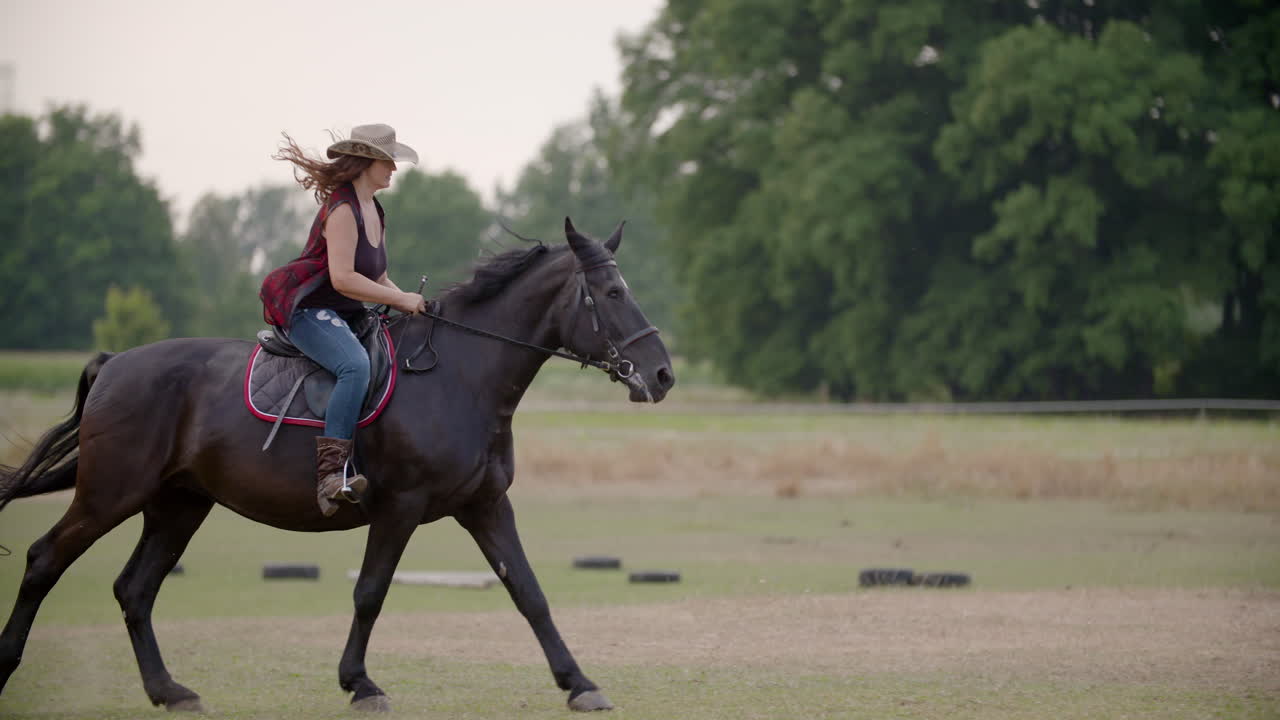 Kvinne med cowboyhatt rir hest på åpen mark