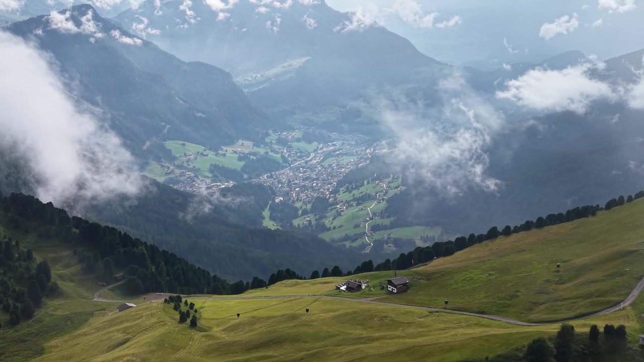 Vista aerea con drone dei dolci prati alpini del Seceda che si affacciano su Ortisei, sotto una luce solare spettacolare e nuvole alla deriva nelle Dolomiti, Italia.