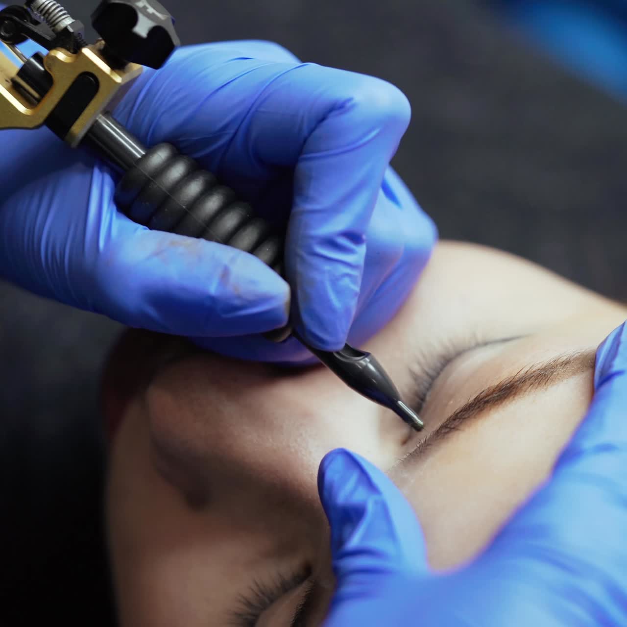 A specialist makes eyebrow tattoo with using a professional machine of permanent makeup in a beauty studio. Close-up