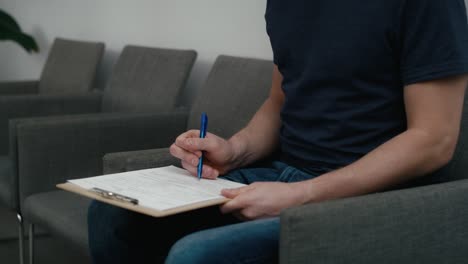 unrecognizable man sitting in waiting room and filling some documents