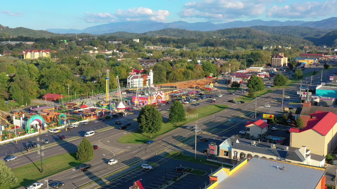 Vibrant drone footage showcases a bustling theme park, featuring thrilling roller coasters and rides set against the Great Smoky Mountains