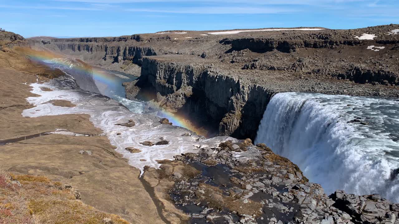 The dry and rocky Icelandic landscape around Dettifoss, wich is one of the most powerful waterfalls in Europe, on a sunny day with a beautiful rainbow appearing in the sky